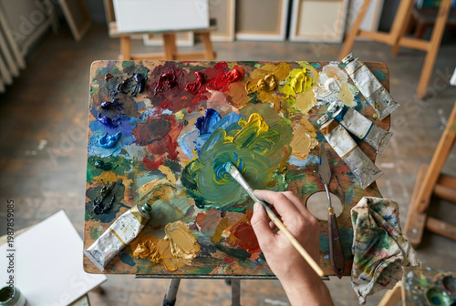 An artist mixing colorful oil paints on a wooden palette with a brush in a creative art studio