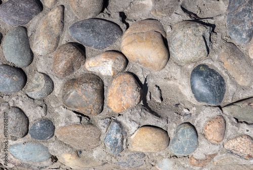 Round yellow gray and dark stones embedded in concrete surface decorative stone texture background.