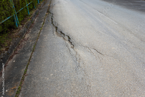 Fotografie Damaged asphalt road with cracks and deteriorated surface near curb, infrastructure problem and road maintenance concept