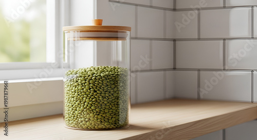 Glass jar filled with dried green lentils on a wooden kitchen counter against a tiled wall in natural light clean style
