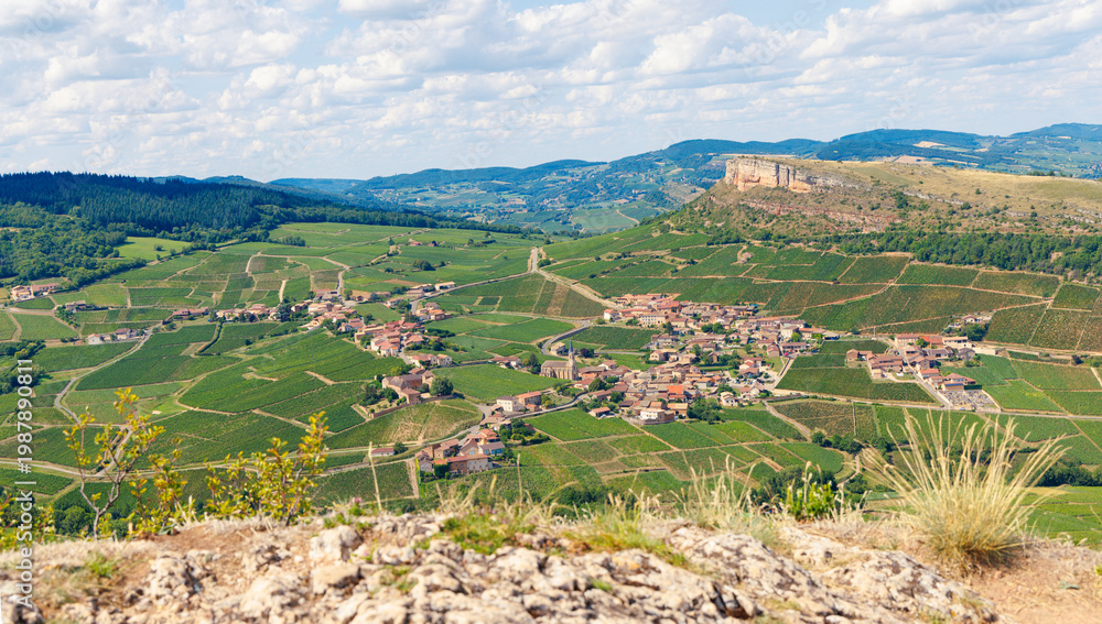 Fototapeta premium High angle panorama of Solutre-Pouilly village and vineyards from the Rock of Solutre, Burgundy, France. Iconic limestone escarpment landscape in Mâconnais wine region under summer sky.