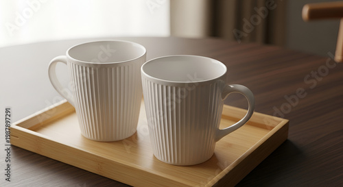 Two elegant white ceramic mugs with vertical ribbing detail on a light bamboo tray set against a warm wooden table and neutral background