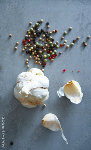 Whole and peeled garlic cloves with vibrant scattered peppercorns on dark stone. Professional culinary background for recipes, menus, and food blogs.