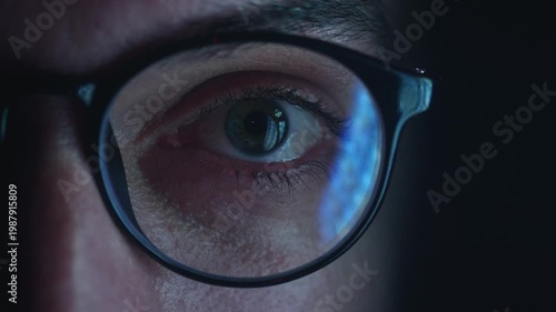 Close up of male eye in glasses reflecting fast scrolling smartphone news feed at night. Man reads breaking news and endless information stream, concept of information overload digital media addiction