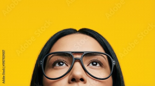 Curious woman looking up with glasses on yellow background