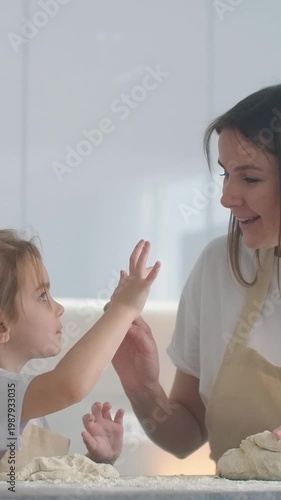Smiling mother and young daughter happily kneading dough together in a bright home kitchen, sharing a joyful baking moment and learning experience