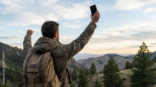 Young hiker celebrating success while holding a smartphone on a mountain summit with a scenic view