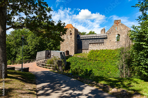 Drone aerial view of Sigulda Castle ruins located in Sigulda, Latvia, within the scenic Gauja National Park. The medieval stone fortress stands on a hill surrounded by dense green forest.