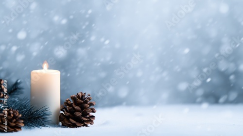 Lit candle beside pinecones on snow-covered surface under falling snowflakes. Blue blurred background