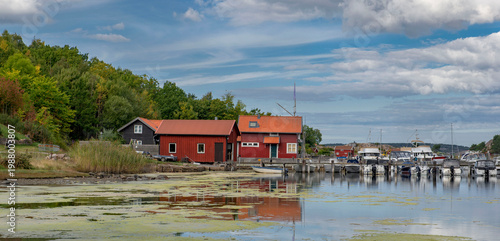 traditional red cabin in Fjalbacka village on a pontoon in front of the sea with boats in marina under sky in sweden