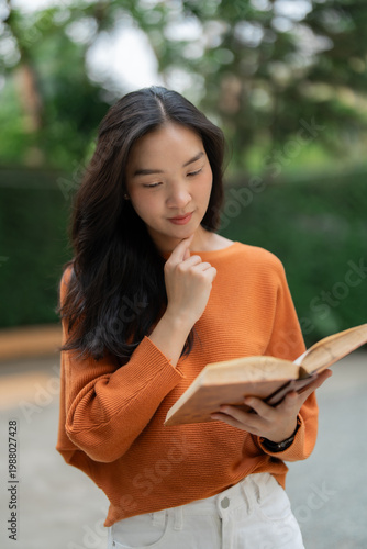 Fotografie Young asian woman reading book outdoors, learning and reflecting