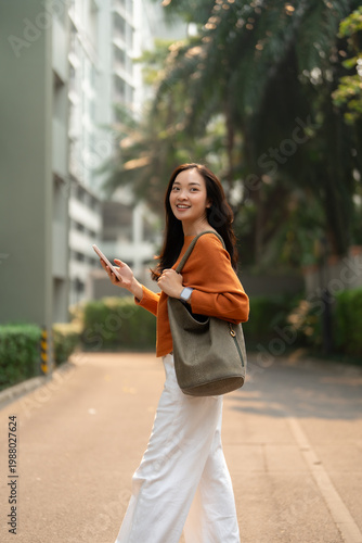Young asian woman walking in city holding smartphone