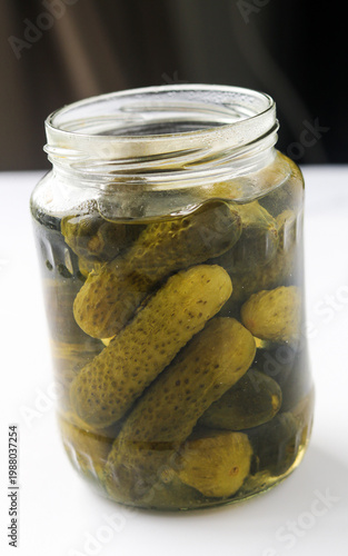Принти на полотні Close-up view of a jar of pickles submerged in brine, showing whole cucumbers and glossy texture, displayed on a dark background
