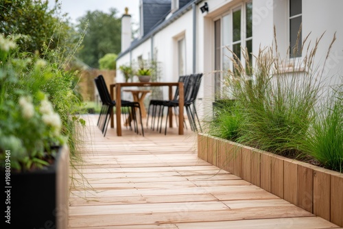 Inviting wooden deck path to an outdoor dining set next to a white house and greenery