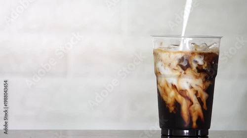 4K Close-up of iced coffee mixed with milk creating beautiful swirl texture Refreshing beverage, Concept ideal for cafe drink menu.