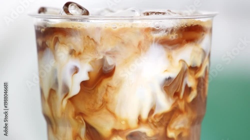 4K Close-up of iced coffee mixed with milk creating beautiful swirl texture Refreshing beverage, Concept ideal for cafe drink menu.