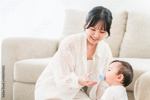 Photos A mother gives her baby water from a bottle in the living room of her home
