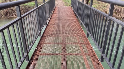 Wallpaper Mural A weathered metal bridge with a rusty grate floor stretches across moving green water. The sturdy black railings offer a sense of safety against the wild, flowing river below. Torontodigital.ca