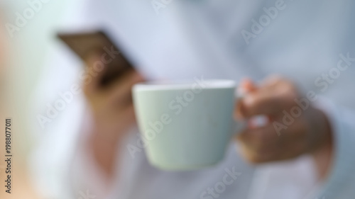 Quadro em tela Holding a warm cup of coffee, a person relaxes while scrolling through their phone, surrounded by soft morning light that brings a peaceful start to the day