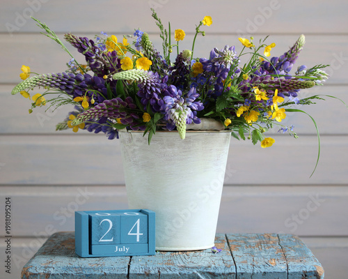 July 24. date of summer day and new beginning. a wooden calendar and a bouquet of lupines and buttercups in decorative bucket.