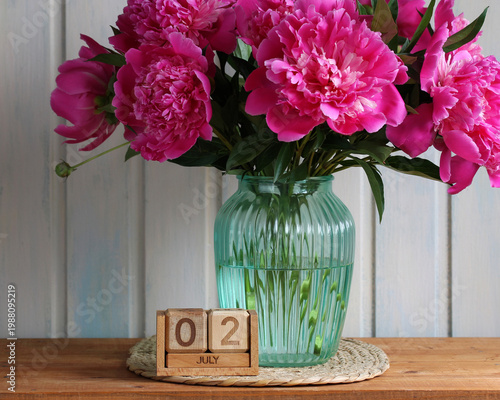 July 2. date of the summer day or holiday event. a wooden calendar and a bouquet of garden peonies in the cottage.