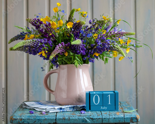 July 1st. date of summer day and new beginning. a wooden calendar and a bouquet of lupines and buttercups in a jug.
