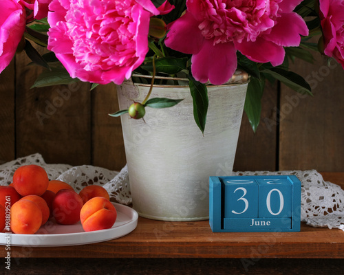 July 30th. the date of the summer day or holiday event. a calendar and a bouquet of garden peonies in a vase on a table in the cottage.