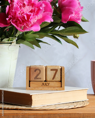 July 27. the date of the summer day or holiday event. a wooden calendar and a bouquet of garden peonies on a table in the cottage.