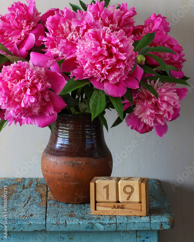 June 19th. a calendar and a bouquet of garden peonies in a vase on a table in the cottage. summer holiday, event or deadline.