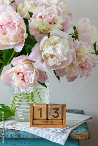 March 13th. a calendar and a bouquet of light garden peonies in a vase. a spring holiday event or birthday.