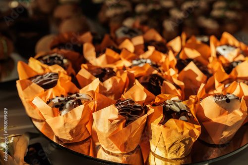 Fotografia Close-up of decadent chocolate muffins with icing drizzle on a mirrored surface at a sophisticated evening banquet