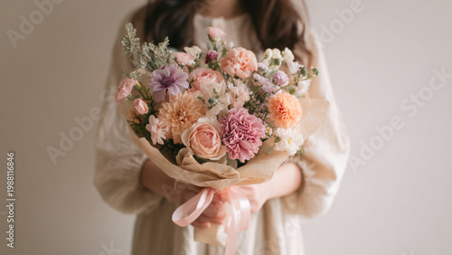 a person facing front holding a vibrant, multicolored bouquet of flowers wrapped in kraft paper and tied with pink ribbons, flowers include roses, carnations, and chrysanthemums