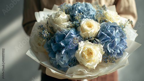 a bouquet of blue hydrangeas and white roses, wrapped in paper and held by an asian woman wearing casual attire. the background is gray with soft lighting, creating a romantic atmosphere. it was taken