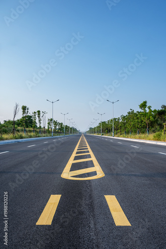 Empty Modern Asphalt Highway with Yellow Centerline and Streetlights Under Clear Blue Sky