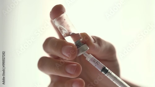 Medical professional aspirating medicine from a glass vial into a syringe against a white background