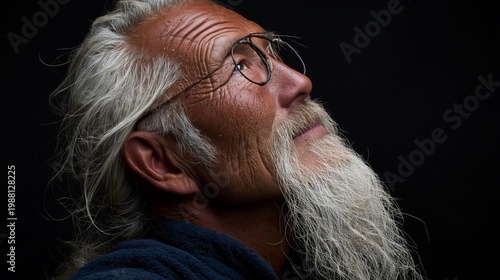 Senior man with long white hair and beard gazes upward. Wearing glasses, he appears thoughtful or inspired. Dark background highlights his face and expressive features. Ideal for stories of wisdom
