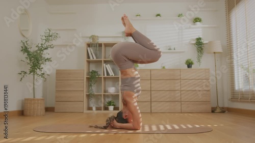 Asian woman yoga inversion pose in bright home interior, calm balance, focused body strength, headstand and forearm stand wellness practice