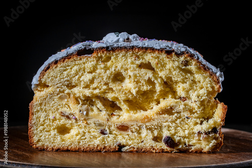 Sliced traditional Easter paska cake or panettone with white icing and raisins on a wooden board against a dark background. Great for festive food and holiday concepts