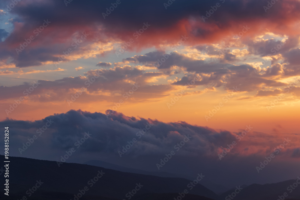Obraz premium Calm evening sky with soft golden light and layered clouds above dark mountain silhouettes in Georgia, creating a peaceful and atmospheric landscape. 