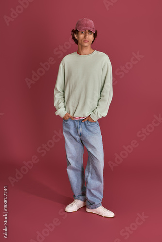 Schilderij op canvas Stylish young man showcases modern fashion against a vivid maroon backdrop