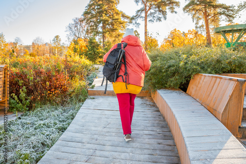 Active lifestyle for overweight. Woman walking on wooden boardwalk with backpack in autumn park. Hiking for health and wellness.
