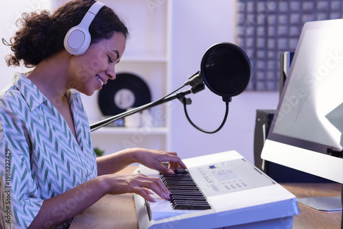 Slika na platnu Young African-American woman with headphones playing synthesizer in recording st