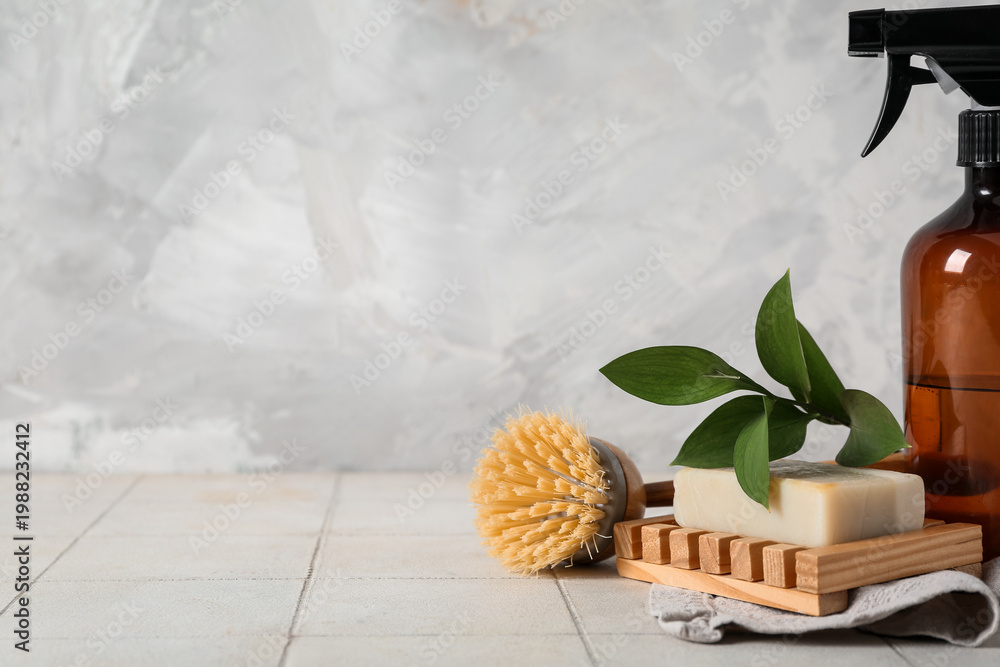 Obraz premium Spray bottle with plant branch, soap and cleaning brush on table near grunge wall