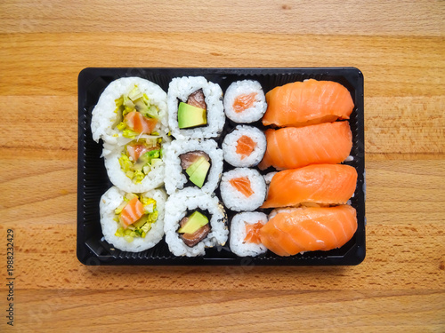 Sushi set in plastic container. Salmon Sushi Rolls Box, Nori Maki, Nigiri Sushi Roll and uramaki rolls on wooden Background 
