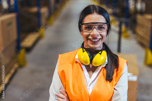Smiling Female Warehouse Worker Wearing Safety Vest and Ear Protection in Logistics Facility