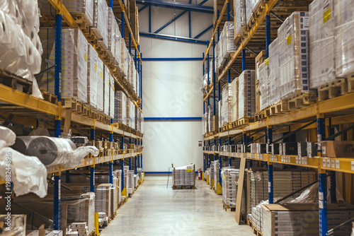 Large Industrial Warehouse Interior With Pallet Racking and Stacked Boxes In Aisle
