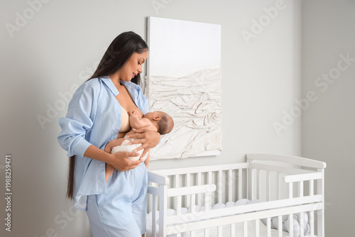 Beautiful young woman breastfeeding her baby in bedroom at home