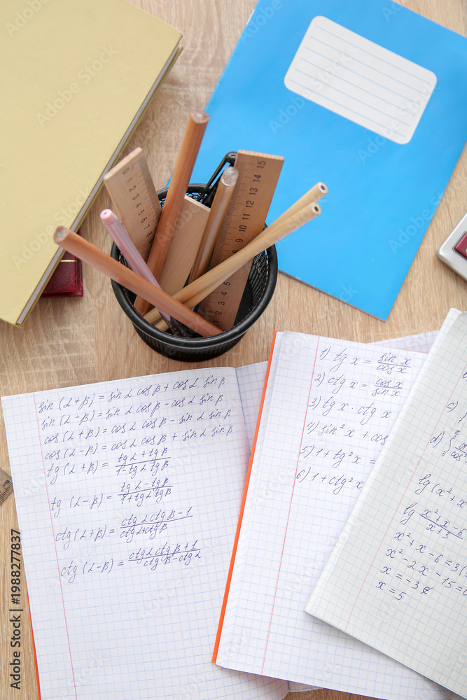 Fototapeta premium Open copybooks with math formulas and stationery on wooden table