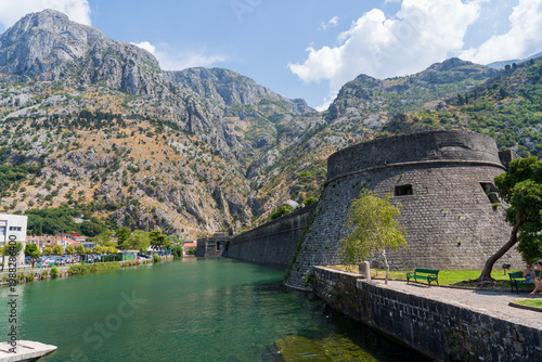 Kotor, Montenegro — August 19, 2025: View of the ancient stone fortress walls and Kampana Tower in the Old Town of Kotor next to the Skurda river against the backdrop of high rocky mountains.