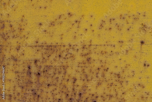 Close-up of weathered yellow painted metal surface with heavy rust spots and industrial corrosion texture